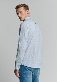 Chemise à manches longues bleu clair avec une texture à motifs, poignets boutonnés et col pointu, associée à un pantalon en denim bleu.