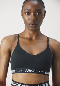 Crni sportski grudnjak s tankim trakama i V-izrezom. Ima široku elastičnu traku s bijelim Nike logotipom na dnu. Glatka tekstura.