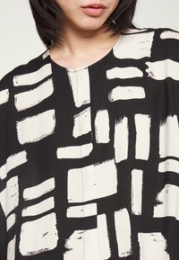 Svart och vit topp med ett penseldragsmönster, rund halsringning och lös passform, tillverkad av ett lättviktigt tyg.