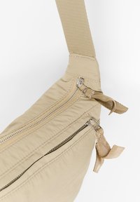 Borsa a tracolla in tessuto beige con due scomparti con zip, tracolla testurizzata e dettagli in metallo sui lati. Materiale morbido con dettagli cuciti.