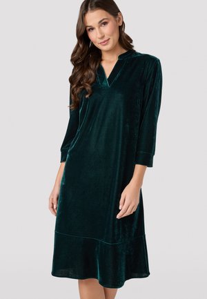 Velvet dress in dark green featuring three-quarter sleeves, a V-neckline, and a flared hem. Soft texture with subtle sheen.