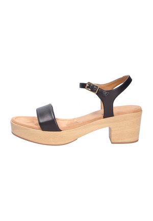 Sandal de cuero negro con una correa ancha, hebilla ajustable en el tobillo y un tacón de bloque de madera beige para estabilidad y soporte.