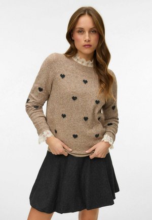 Brun sweater med sorte hjerte mønstre, med blonde detaljer ved halsudskæringen og manchetten. Bærer et mørkegråt nederdel, med en flæset form.