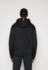 Μαύρο φούτερ με κουκούλα από μαλακό ύφασμα, με μεγάλη κουκούλα, υφασμένα επιθέματα στους αγκώνες και υφασμένη επένδυση στη μέση με λεπτομέρεια λογότυπου.