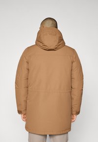 Brun polstret jakke med hette, med rett snitt og lommer på sidene. Laget av mykt, glatt stoff med en lett teksturert overflate.