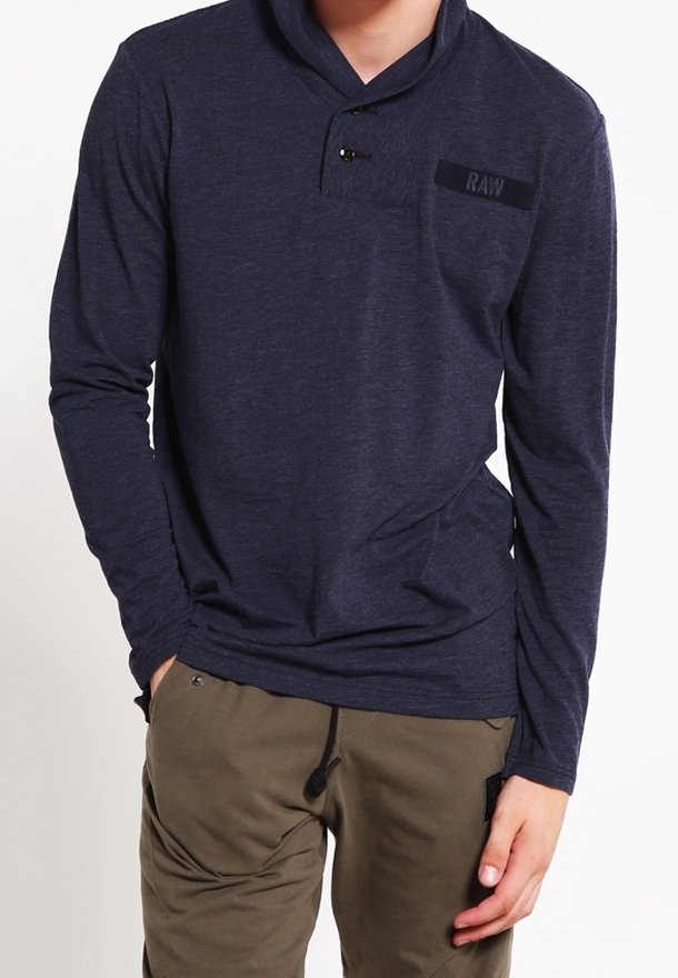 Marinblus med lång ärm och sjalkrage, försedda med en knapp och en bröstficka med texten "RAW" i mörkt tyg.