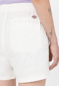 Biele bavlnené šortky s elastickým pásom, zadnou vreckom a malou nášivkou loga Dickies na pravej strane. Hladká textura.