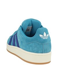 Turkise ruskindsneakers med lila striber, polstret krave, hvidt logo på hælen og en struktureret gummisål.