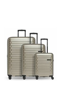 Ensemble de trois valises rigides métalliques argentées avec des accents noirs. Les caractéristiques incluent des lignes horizontales texturées et des poignées rétractables.
