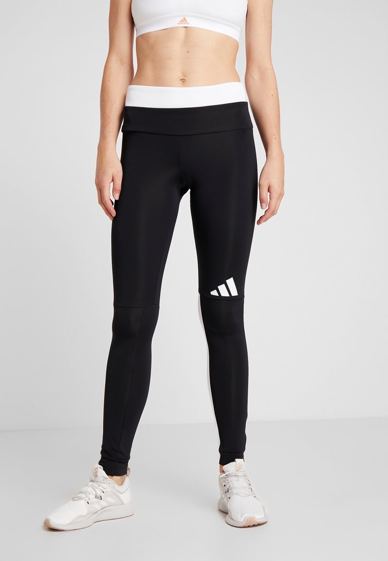 Czarne legginsy z wysokim stanem, wykonane z elastycznego materiału, z białym logo adidas na dolnej lewej nogawce.