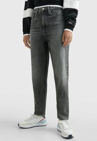 Jeans de mezclilla gris con corte recto y acabado desgastado. Combinados con zapatillas blancas con detalles en azul y rojo.
