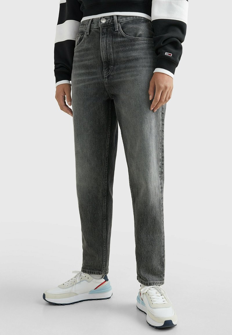 Jeans de mezclilla gris con corte recto y acabado desgastado. Combinados con zapatillas blancas con detalles en azul y rojo.