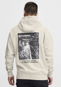 Cream-colored hoodie featuring a black graphic print on the back, depicting a tunnel with a straight pathway and text below the image.