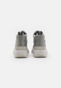 Baskets imperméables grises avec une tige rembourrée, un talon texturé et une languette. Elles présentent une semelle blanche contrastante et un branding discret sur le côté.