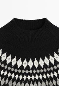 Pull noir en tricot avec col montant côtelé et motif géométrique en losanges blancs et gris sur la poitrine.