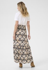 Gonna maxi con un motivo a foglia di palma bianco e nero, design a strati e vita elastica, abbinata a una maglietta bianca semplice e stivali con tacco marroni.