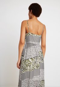 Svart- och vitmönstrad klänning med gröna accenter; har spaghettiband och en flödande silhuett med lager på lager-design.