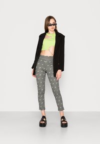 Top verde cropped com recorte, blazer preto, calças slim-fit padrão e sandálias pretas chunky. Acento de corrente prateada na cintura.