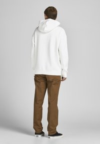 Witte katoenen hoodie met een trekkoordkap, gecombineerd met bruine broek en zwarte schoenen, gezien vanaf de achterkant. Eenvoudig, ontspannen ontwerp.