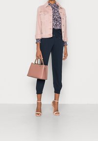 Jasnoróżowa dżinsowa kurtka, wzorzysta granatowa bluzka, granatowe spodnie dresowe, różowa torebka oraz beżowe sandały na obcasie. Gładkie tekstury i luźny krój.
