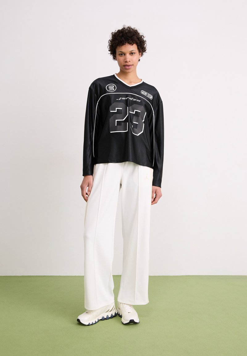 Camisa negra de manga larga con acentos blancos, con el número 23 y un logotipo gráfico. Combinada con pantalones holgados blancos y zapatos deportivos.