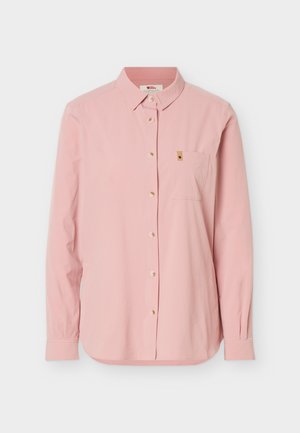 Camisa de manga larga color rosa claro con botones, cuello y bolsillo en el pecho que tiene una pequeña etiqueta marrón, sobre fondo blanco.