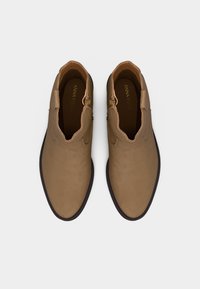 Ζευγάρι ταμπά σουεντ μποτάκια αστραγάλου με στρογγυλές μύτες και μαύρες σόλες, σε θέα από πάνω σε λευκό φόντο.