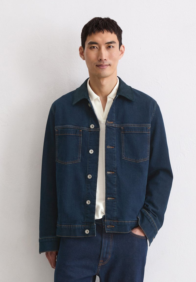 Donkerblauwe spijkerjack met een kraag, knoopsluiting en twee borstzakken. Beschikt over contrasterend stiksel en een losse pasvorm.