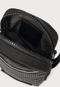 Kompakt fekete hátizsák texturált szürke aljjal, cipzáras záródással és belső címkével. Simább nejlon külsővel és masszív fém részekkel rendelkezik.