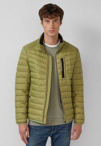 Jasnozielona, pikowana kurtka z wysokim kołnierzem, kieszenią na piersi na zamek błyskawiczny oraz czarnymi akcentami, zestawiona z jasnoszarą bluzą pod spodem.