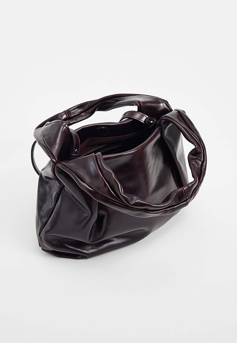 Sac à main en cuir brun avec une texture douce et froissée, une grande ouverture et deux poignées arrondies. Présente un design minimaliste et aucun matériel proéminent.