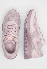 Zapatillas Nike en malla rosa claro con una parte superior texturizada, punta redondeada, suela acolchada y acentos translúcidos. Presenta un sistema de cierre con cordones.