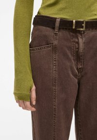 Rjave denim hlače s sprednjimi žepi in temno rjavim semiš pasom. Zgornji del je oprijet dolg rokav v olivno zeleni barvi iz bombaža.