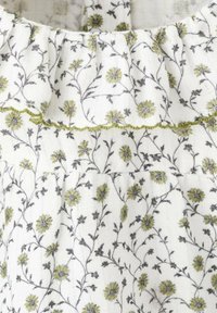 Biely textilný top s kvetinovým vzorom v zelenej a šedej farbe, s volánovým výstrihom a textúrovanými vyšívanými detailmi.