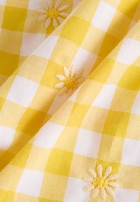 Tissu à carreaux jaunes et blancs avec une finition texturée, présentant des fleurs brodées dans un jaune plus clair à intervalles réguliers.