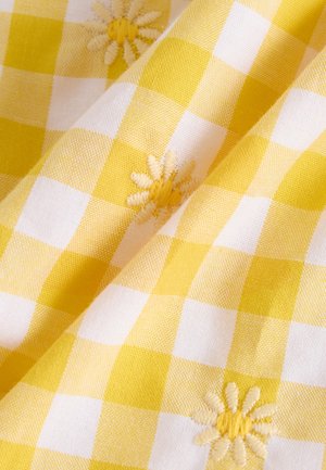 Geltonos ir baltos ekrano audinio raštas su tekstūriniu baigimu, kuriame reguliariais intervalais siuvinėti gėlės šviesiai geltonos spalvos.