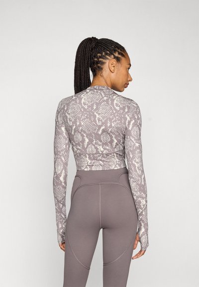 Langermet tettsittende topp med slangeskriftmønster i lys grå og off-white toner, kombinert med høyt liv, glatte, taupe leggings.