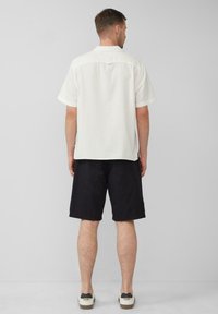 Lichtgekleurde linnen overhemd met korte mouwen en een rugpand-detail, gecombineerd met donkere shorts en casual sneakers. Eenvoudig en casual ontwerp.