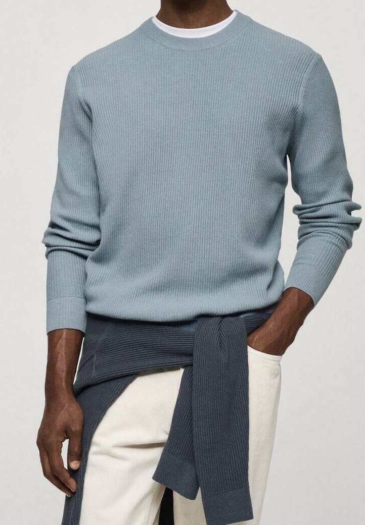 Homme portant un pull léger côtelé bleu clair avec un pull côtelé bleu foncé noué autour de la taille, associé à un pantalon blanc cassé.