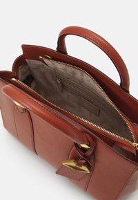 Sac à main en cuir marron texturé avec ferrures dorées, double poignée et fermeture éclair ; intérieur avec doublure de marque et compartiments.