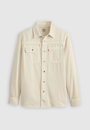 Hemd mit Knopfleiste aus cremefarbenem Stoff, ausgestattet mit zwei Brusttaschen, einem spitz zulaufenden Kragen und Metallknöpfen. Glatte Textur mit Nähdetails.