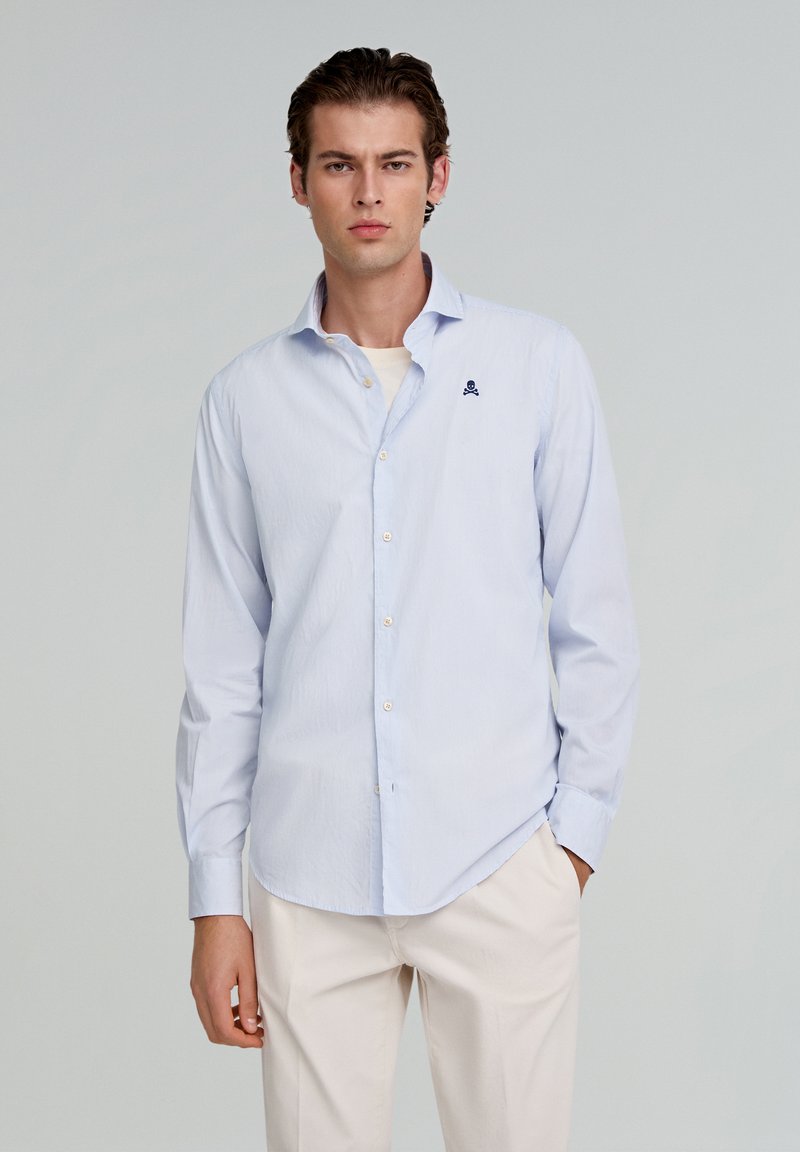 Helleblaue gestreifte Button-Down-Bluse mit langen Ärmeln, die ein kleines dunkelblaues Logo auf der Brust trägt. Hergestellt aus einem glatten, leichten Stoff.