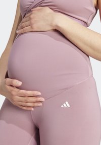 Raskaidessu naisten urheiluvaatteet pehmeästä vaaleanpunaisesta kankaasta, joissa on kiinteä muotoilu. Valkoinen logo korostaa vyötäröä. Sujuva pinta.