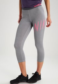 Graue Nike Pro Leggings mit engem Schnitt, mittlerer Wadenlänge und einem großen rosa Logo an der Seite. Glatte Textur und elastischer Bund.