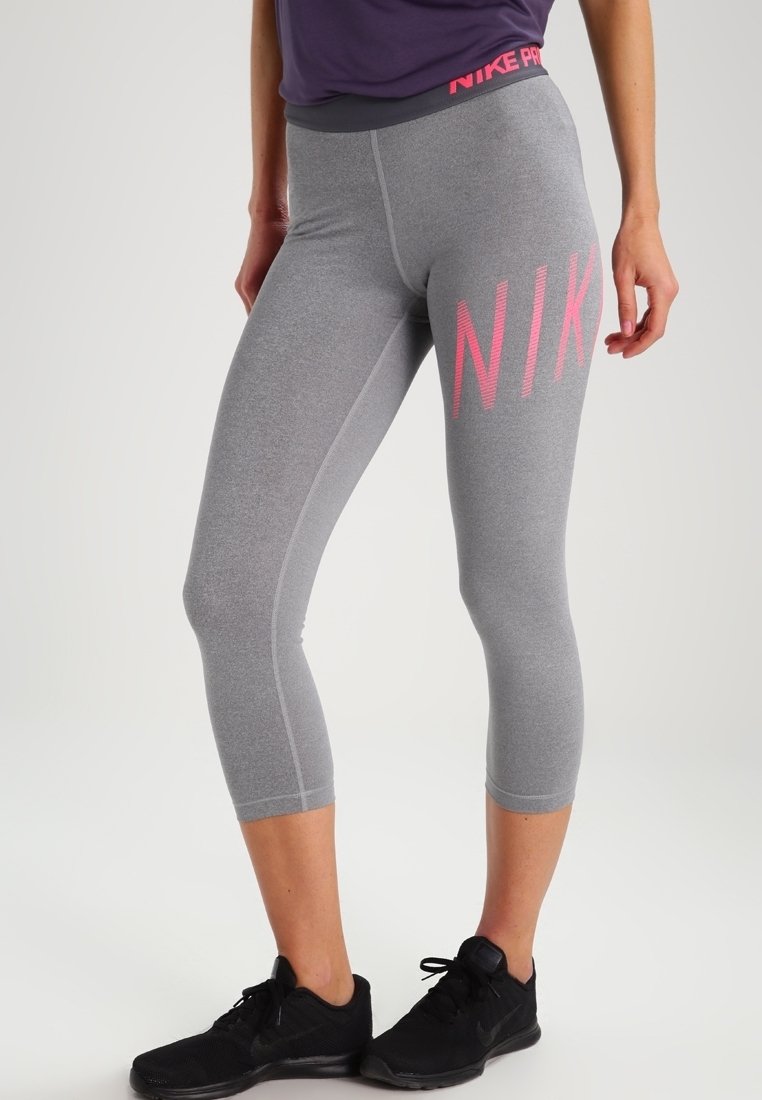 Graue Nike Pro Leggings mit engem Schnitt, mittlerer Wadenlänge und einem großen rosa Logo an der Seite. Glatte Textur und elastischer Bund.