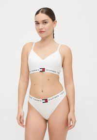Wit bh en stringset met een V-halsontwerp, verstelbare bandjes en een gebrandmerkte elastische tailleband met logo-accenten. Glad textuur.
