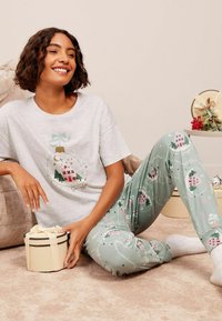 Šedé tričko s grafikou domu a zelené pyžamové kalhoty s růžovými domy a spirálami. Pohodlná tkanina s volným střihem. Vedle dárková krabička.