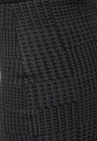Leggings noirs présentant un motif texturé avec des designs géométriques contrastés. Fabriqués dans un matériau extensible, conçus pour le confort et la flexibilité.