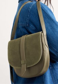 Borsa a tracolla verde oliva con un flap in tessuto testurizzato e corpo in pelle liscia, dotata di una tracolla e dettagli di cucitura discreti.