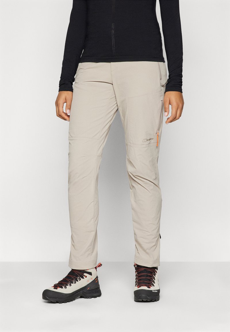 Pantalons d'extérieur légers beiges avec une poche zippée sur la cuisse, associés à des bottes de randonnée noir et blanc avec des lacets rouges.